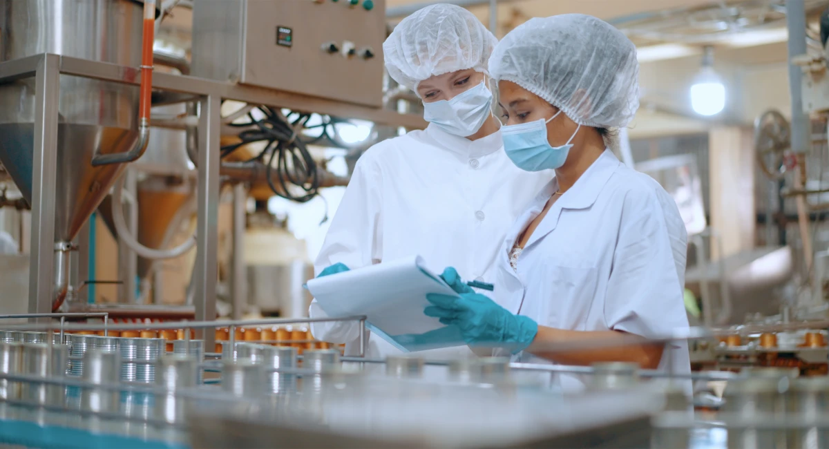 Two women in hair nets and face masks inspecting a food production line