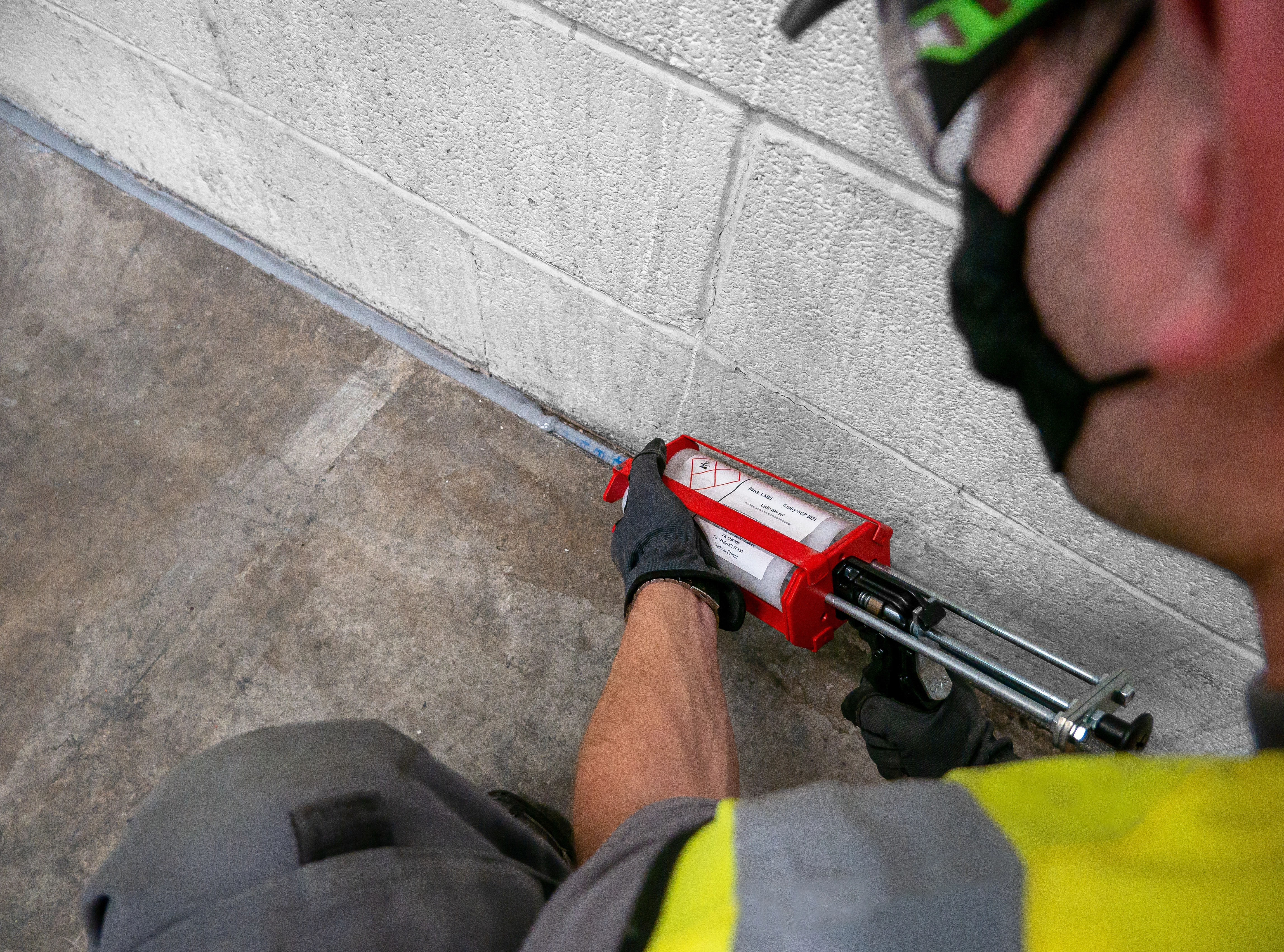 A pest control technician applies a Flexi Armour sealant to a gap in a building
