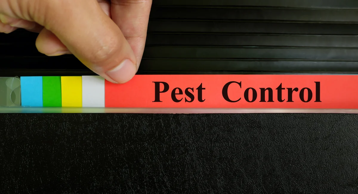 A hand picking a file labeled “pest control” from a black binder folder